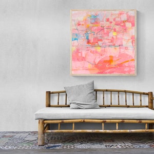 May include: A light pink abstract painting in a wooden frame hangs above a light gray cushioned daybed with a bamboo frame.