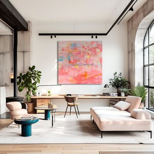 May include: Abstract painting in shades of pink, orange, and yellow with geometric shapes and lines. The painting is hanging on a white wall in a modern living room with a couch, coffee table, and plants.
