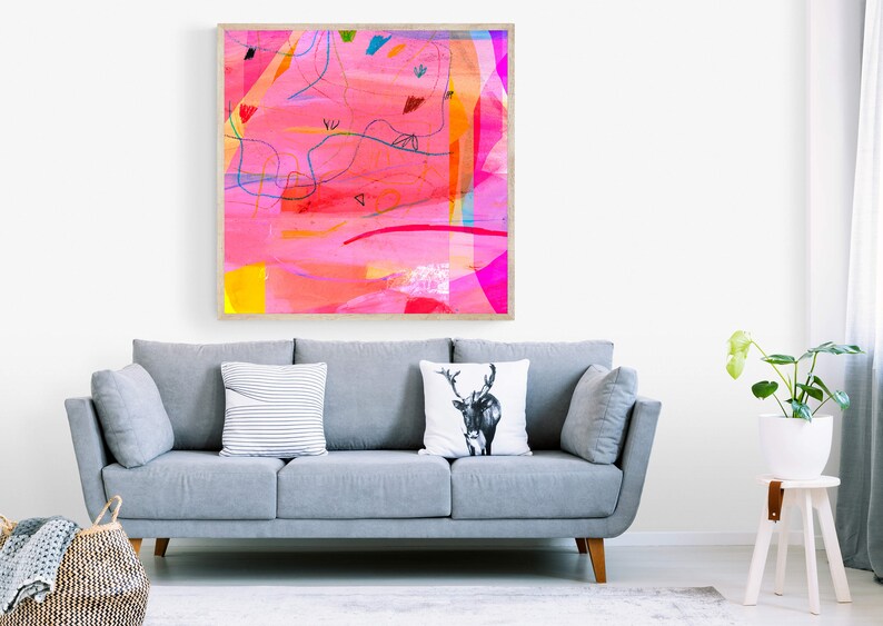 May include: A framed abstract painting with pink, yellow, blue, and red colors. The painting is in a wooden frame and is hanging on a white wall above a gray sofa.