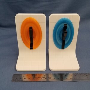 May include: Two white bookends with orange and blue circular designs. Each design has a black 3D printed figure in the center.