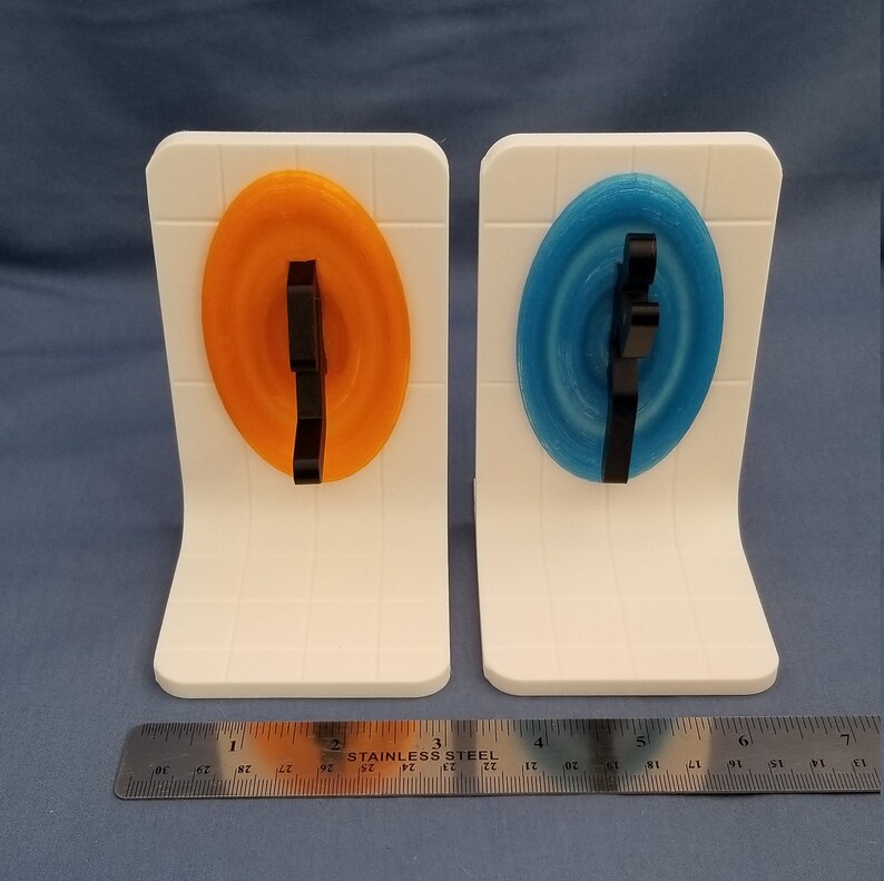 May include: Two white bookends with orange and blue circular designs. Each design has a black 3D printed figure in the center.