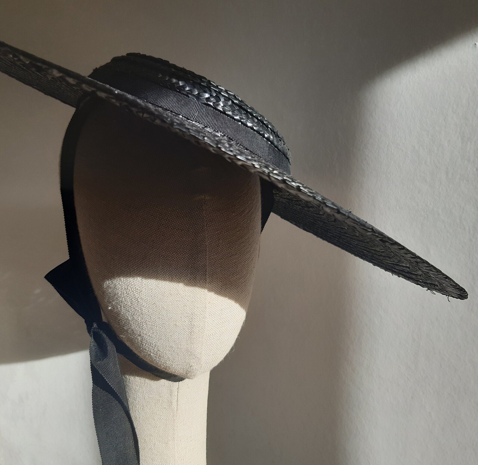 Shadowy side view of black straw sun hat with ribbon tie, a maximalist take on summer goth fashion with Victorian edge.