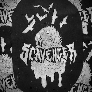 May include: Black and white patch featuring a stylized bird with the word "Scavenger" in a dripping font. Several flying birds are above the bird's head. The patch has an oval shape and is likely for clothing or accessories.