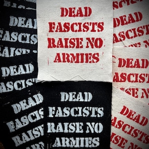 May include: A collection of fabric patches with the text "DEAD FASCISTS RAISE NO ARMIES" printed in red and white. Some patches are black with white text. The patches are arranged in a slightly overlapping pattern.