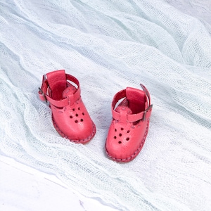 May include: A pair of pink leather sandals with straps and buckles. The sandals have a decorative pattern of small holes.
