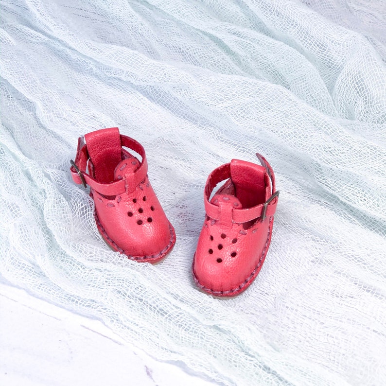 May include: A pair of pink leather sandals with straps and buckles. The sandals have a decorative pattern of small holes.