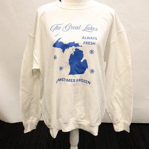 Pu&ograve; includere: Felpa bianca con grafica blu dei Grandi Laghi, compreso lo stato del Michigan. Il testo recita "The Great Lakes, Always Fresh, Sometimes Frozen" con accenti di fiocchi di neve blu. La felpa &egrave; esposta su un manichino bianco.