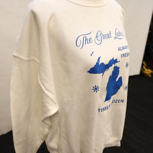 Pu&ograve; includere: Felpa color crema con grafica blu dei Grandi Laghi e testo. Il testo recita "The Great Lakes, Always Fresh, Times Frozen". La felpa ha un girocollo e maniche lunghe.