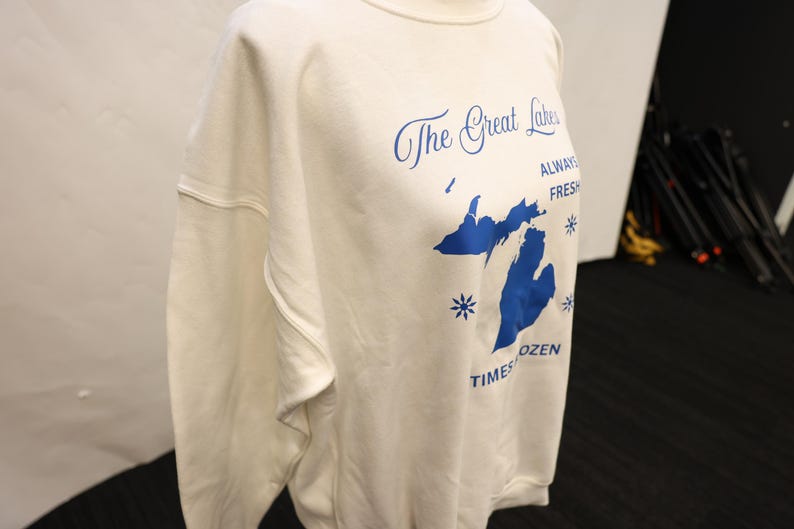 Pu&ograve; includere: Felpa color crema con grafica blu dei Grandi Laghi e testo. Il testo recita "The Great Lakes, Always Fresh, Times Frozen". La felpa ha un girocollo e maniche lunghe.