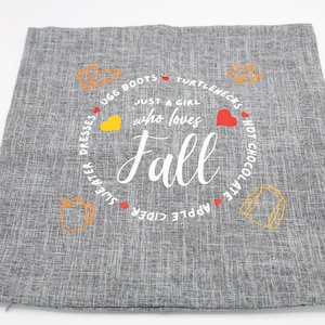 May include: Gray decorative pillow with the text "Just a girl who loves Fall" in white script. The design includes a circular border with fall-themed icons and words like "Ugg boots" and "Hot Chocolate".