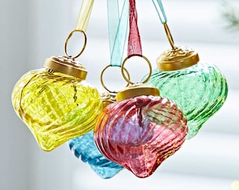 Könnte beinhalten: Eine Hand hält eine Auswahl an herzförmigen Weihnachtskugeln. Die Kugeln sind in Gelb, Blau, Rot und Grün gehalten und haben goldfarbene Metallkappen und Aufhängeschlaufen. Jede Kugel hat eine strukturierte Oberfläche und wird von einem Band gehalten.