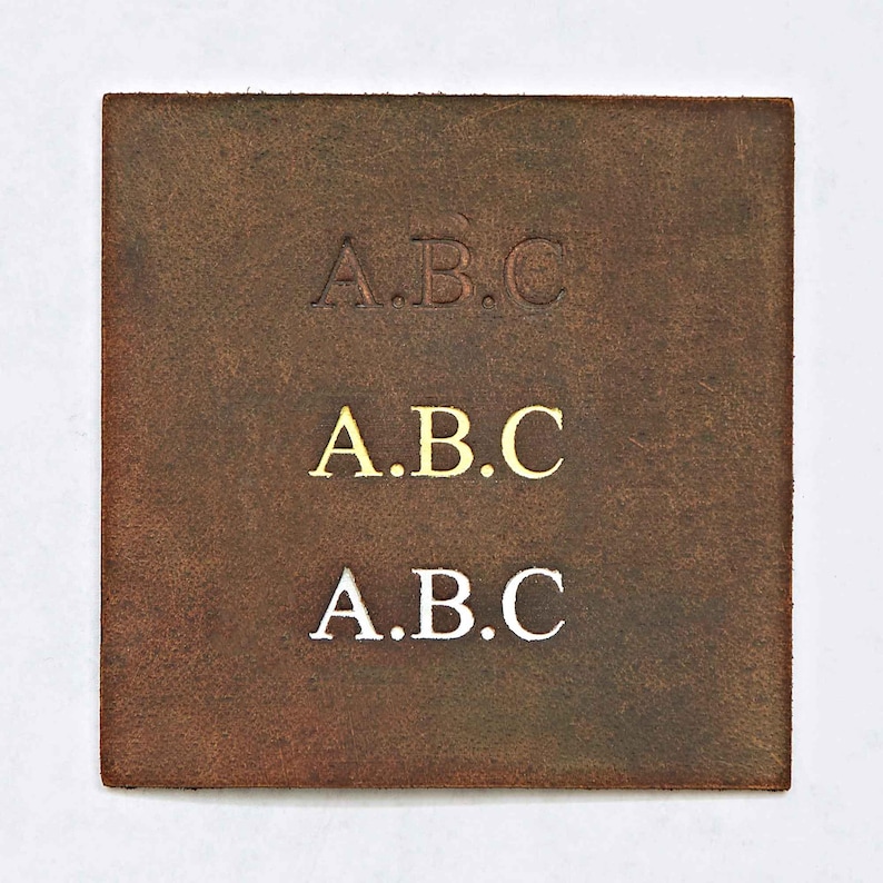May include: A brown leather patch with the letters "A.B.C." embossed in three different colors: dark brown, gold, and white.