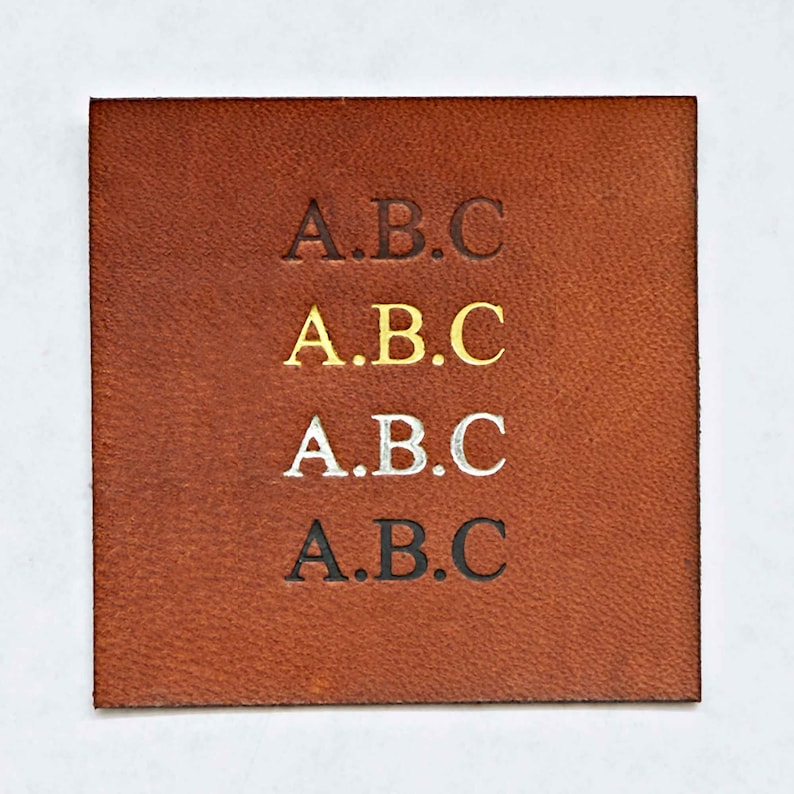 May include: A close-up of a brown leather patch with the letters "A.B.C." embossed in black, gold, silver, and black.