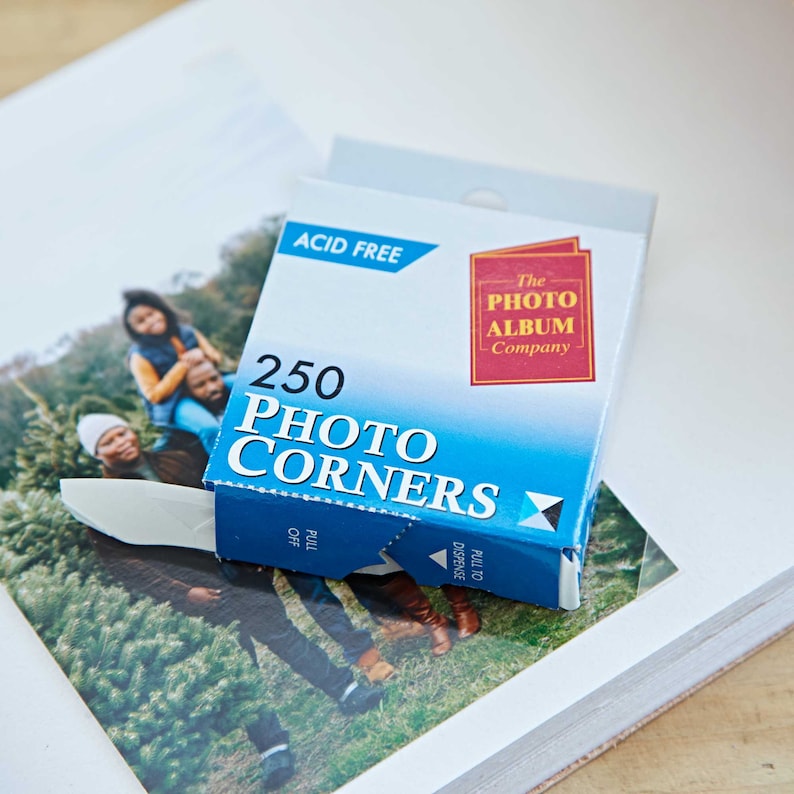 May include: A blue box of 250 acid-free photo corners from The Photo Album Company. The box has a white pull tab and a blue and white dispenser.