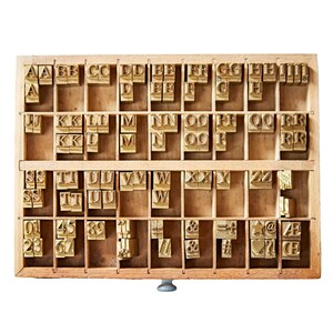 May include: A wooden printing block with a drawer containing metal letterpress type. The type includes letters, numbers, and symbols. The letters are arranged alphabetically in rows.