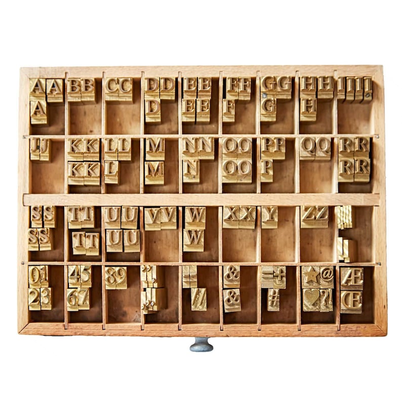 May include: A wooden printing block with a drawer containing metal letterpress type. The type includes letters, numbers, and symbols. The letters are arranged alphabetically in rows.