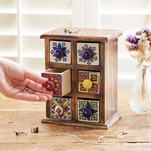 May include: A wooden box with six small drawers, each with a different colorful ceramic tile design. The drawers have ceramic knobs in various colors. The box is sitting on a wooden surface.
