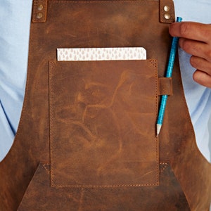 May include: A brown leather apron with a large pocket and a blue pencil sticking out of it.