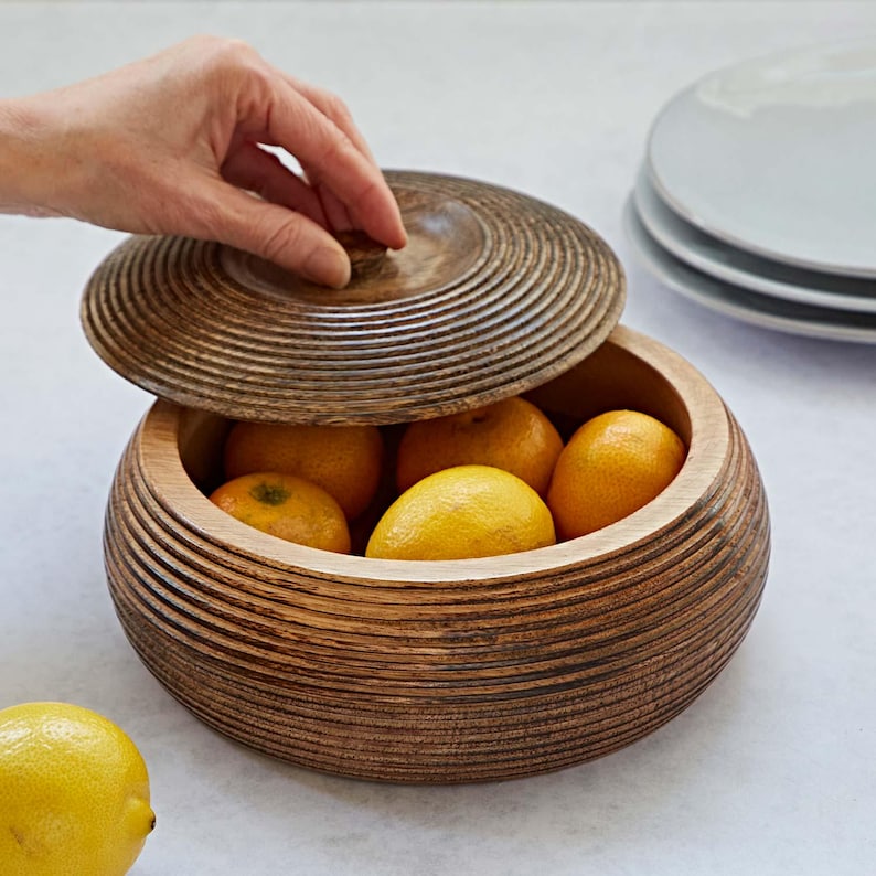 K&ouml;nnte beinhalten: Eine Holzschale mit Deckel, gef&uuml;llt mit Zitronen. Die Schale hat ein gerilltes Design und ist aus dunklem Holz.