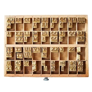 May include: A wooden printing block with a drawer containing metal letterpress type. The type includes letters, numbers, and symbols. The letters are arranged alphabetically in rows.