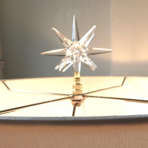 May include: A clear crystal star finial lampshade topper with a gold metal base.