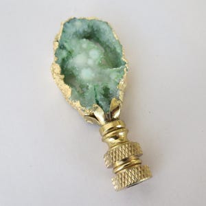 May include: A gold lamp finial with a green agate stone top. The agate has a natural, irregular shape and a white center.