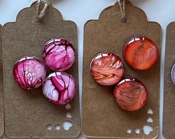 May include: Twelve sets of three small, round, glass cabochons with various abstract designs. Each set is displayed on a brown card with a scalloped edge.