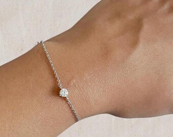 Puede incluir: Un delicado brazalete de cadena de plata con un solo diamante redondo y transparente en el centro.