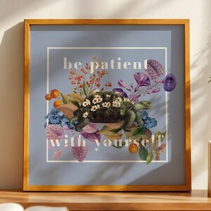 May include: A framed print with a light blue background and a floral design. The text "be patient with yourself" is printed in white on the print.