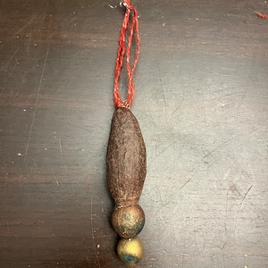 May include: A brown, wooden ornament with a red and white string hanging from the top. The ornament has two gold beads at the bottom.