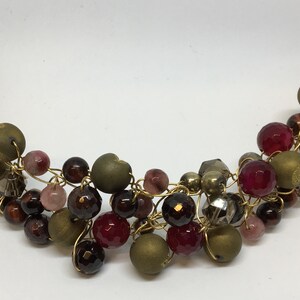 May include: A gold wire necklace with a variety of beads in shades of brown, pink, and red. The beads are arranged in a cascading pattern.
