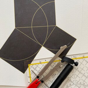 May include: A black and white protractor, a black compass, and a black ruler with yellow markings. The compass is open and the ruler is partially visible. The protractor is on top of the compass and ruler. The protractor has a black and white grid pattern with numbers from 10 to 150. The compass has a black handle and a silver metal arm. The ruler has a black handle and a silver metal arm. The ruler has a yellow scale with numbers from 10 to 150.
