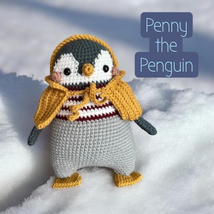 Könnte beinhalten: Eine handgefertigte Häkelpinguin-Puppe namens "Penny the Penguin" mit grauem Körper, gelbem Kapuzenmantel und gestreiftem Hemd. Der Pinguin hat schwarze Augen, einen gelben Schnabel und kleine gelbe Füße. Der Text "Penny the Penguin" steht in einer blauen Box.