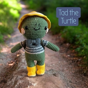 May include: A handmade green crochet turtle doll named Tad, wearing a yellow hat, a gray and white striped shirt, a gray bow tie, and yellow boots. The doll has rosy cheeks and is standing on a path. The text "Tad the Turtle" is in a blue box.