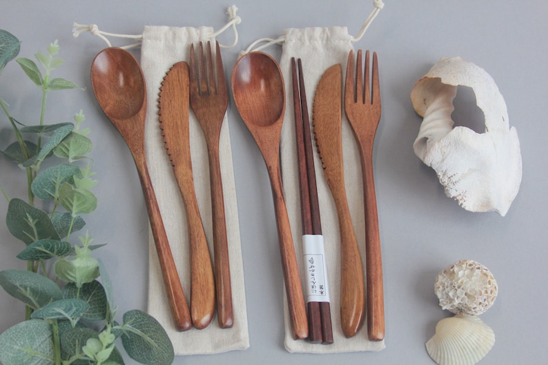 Eco Friendly cutlery set made from wooden bamboo. Set come with either 3 or 4 pieces and come in a cloth bag with a drawstring. Photo details both sets surrounded with green leaves and shells