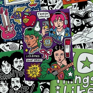 May include: A collection of colorful zines and stickers with illustrations. The central zine features a person with pink hair wearing headphones, holding a phone. Other designs include guitars, apples, and the text "make BAD art."