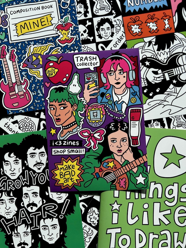 May include: A collection of colorful zines and stickers with illustrations. The central zine features a person with pink hair wearing headphones, holding a phone. Other designs include guitars, apples, and the text "make BAD art."