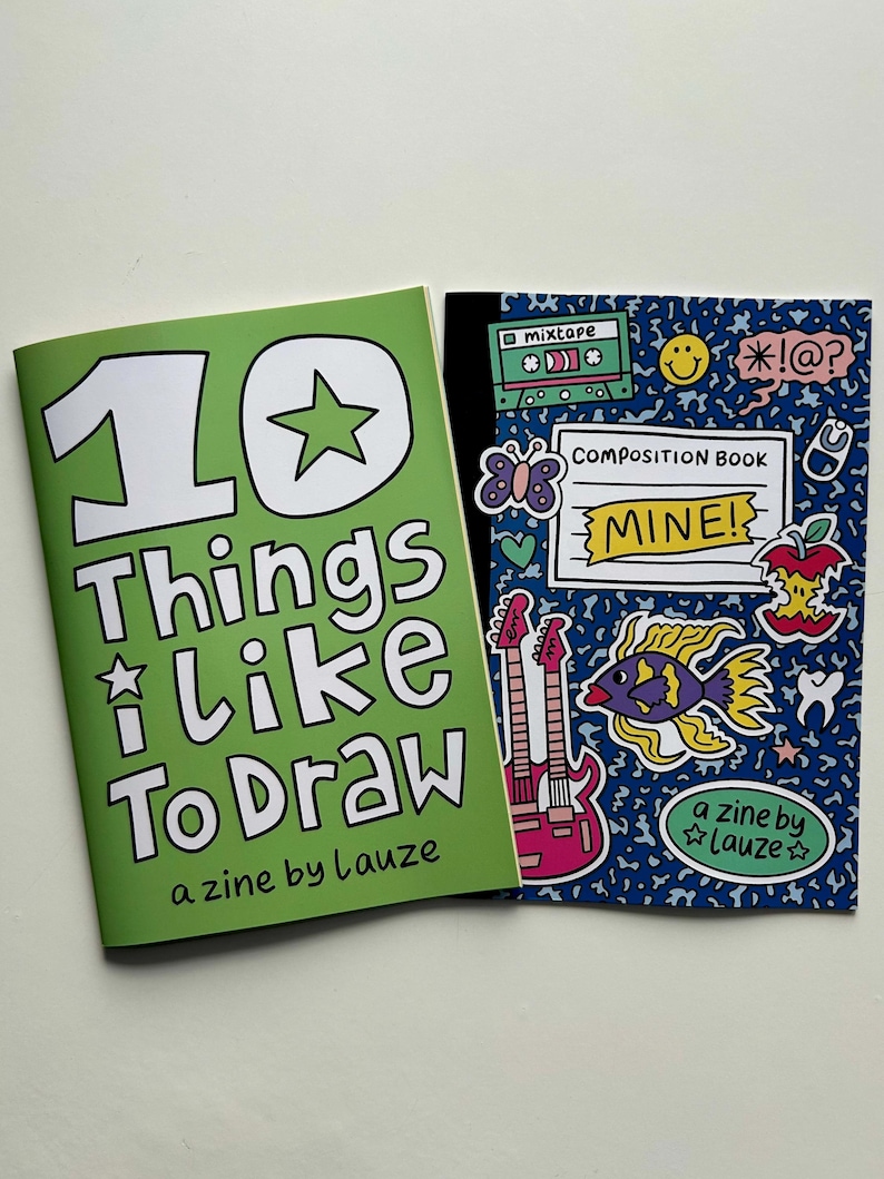 May include: Two zines are displayed. The green zine cover reads "10 Things I Like To Draw" and "a zine by Lauze." The blue zine cover says "COMPOSITION BOOK MINE!" and features a fish, guitars, and other graphics.