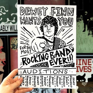 Può includere: Poster in bianco e nero con la scritta "Dewey Finn Wants You" e "For the Most Rocking Band Ever!!!". Un'illustrazione a cartoni animati di un uomo che indica è al centro. La parte inferiore del poster recita "Auditions" con handle di social media.