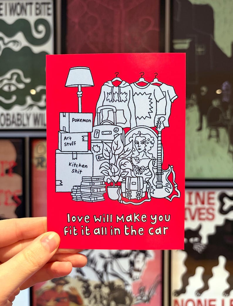 May include: A red art print featuring a black and white illustration of packed boxes, clothes, a lamp, a guitar, and a woman's portrait. The text "love will make you fit it all in the car" is at the bottom.