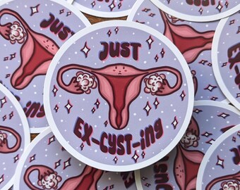 Op de afbeelding: Een set ronde stickers met een cartoonillustratie van een baarmoeder met de tekst "Just Ex-cysting" in een retro-lettertype. De stickers zijn op een paarse achtergrond met witte sterren.