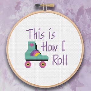 Op de afbeelding: Een witte borduurring met een kruissteekontwerp van een rolstoel met de tekst "This is How I Roll".
