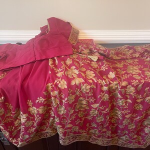 May include: A pink and gold saree with a floral pattern. The saree is made of a soft, flowing fabric and has a delicate gold trim.