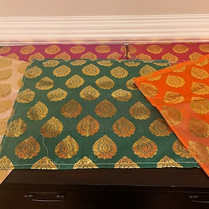 May include: Four placemats with a gold and green paisley pattern. The placemats are made of a woven fabric and have a subtle sheen.