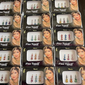 May include: A display of 12 packages of colorful, jeweled, adhesive bindis. Each package has a black background with white text that reads "Fine Touch" and "Fancy Bindi".