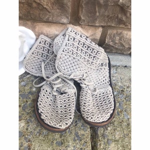 May include: A pair of beige crocheted ankle boots with laces. The boots have a woven pattern and are made of a soft, natural material.