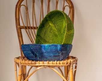 Puede incluir: Dos cestas tejidas, una verde y otra azul, están sentadas en una silla de mimbre. La cesta verde está encima de la cesta azul.