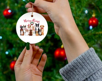 May include: White round Christmas ornament with a red and green wreath and the text "Merry Always".  The ornament features a group of cartoon dogs wearing Santa hats and other festive attire.