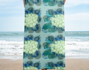 Könnte beinhalten: Ein Strandtuch mit einem abstrakten Muster in Grün-, Blau- und Weißtönen. Das Handtuch wird von einer Person vor einer Strandkulisse gehalten.