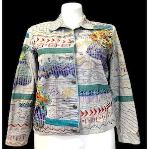 May include: A light gray denim jacket featuring a button-up front, a classic collar, and long sleeves. The jacket is decorated with colorful, intricate embroidery patterns including geometric shapes, wavy lines, and floral motifs in red, blue, green, and yellow.